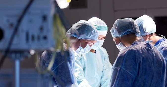 Medical professionals in scrubs stand around an operating table
