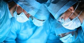 A group of doctors in blue scrubs looking at something not visible in the image