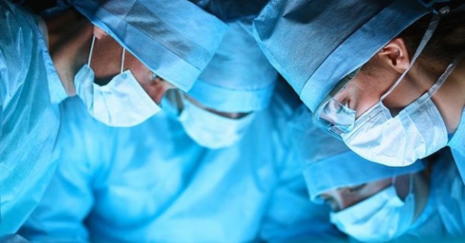 A group of doctors in blue scrubs looking at something not visible in the image