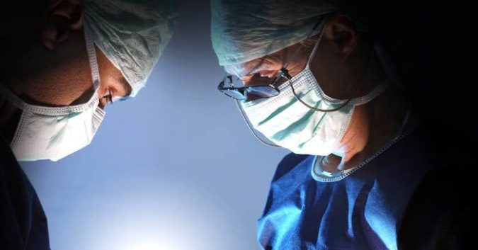 2 masked doctors stand over a patient, presumably during surgery
