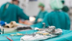 Closeup of sutures with blurry doctors doing surgery in the background