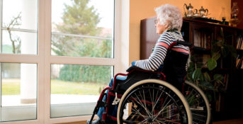 Elderly woman sitting alone ay a window in a nursing home