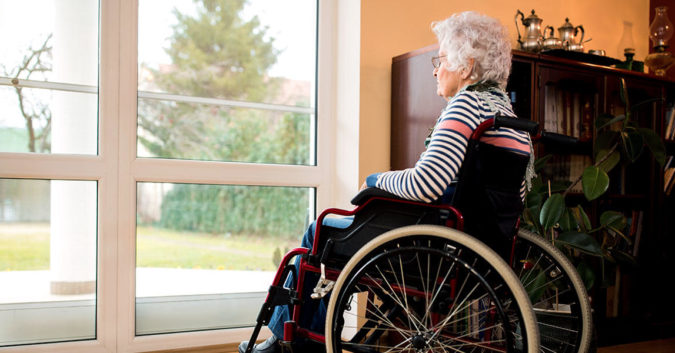 Elderly woman sitting alone ay a window in a nursing home