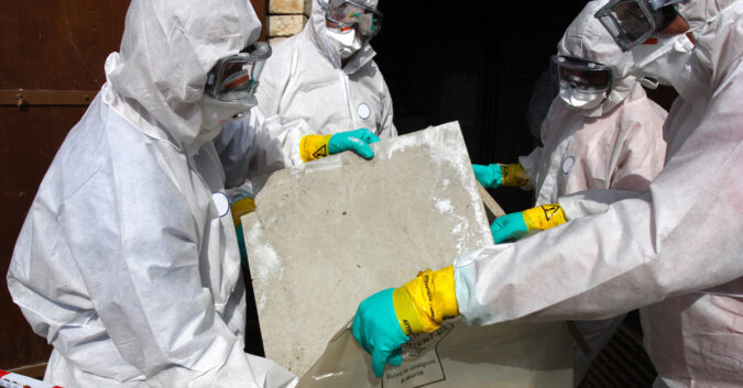 Workers in protective gear remove asbestos from building