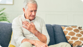 senior citizen on couch with his hand on his heart