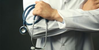 close up photo of a doctor with their arm's crossed while holding a stethoscope