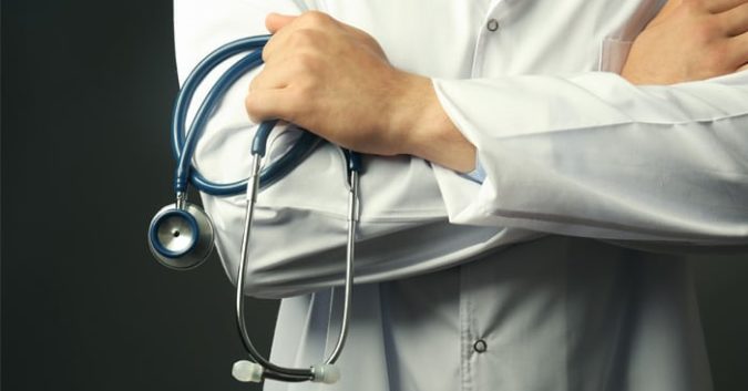 close up photo of a doctor with their arm's crossed while holding a stethoscope
