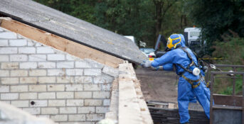 Worker removing asbestos-containing roof material