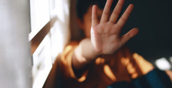 A young boy holds his hand up to block his face