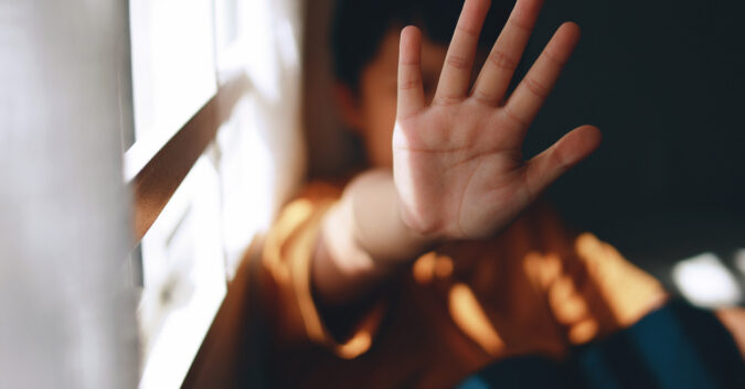 A young boy holds his hand up to block his face