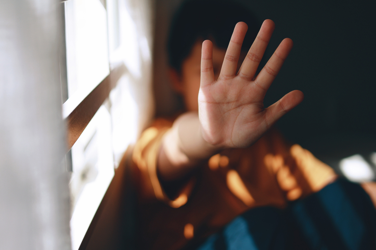 A young boy holds his hand up to block his face