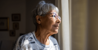 An older woman looks out of a window at a nursing home