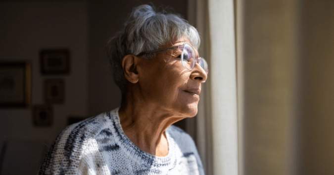An older woman looks out of a window at a nursing home