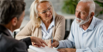 Elderly couple reviewing and signing contract with assistance.