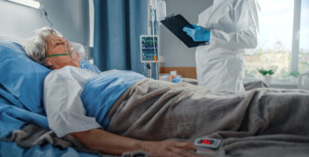 A patient laying in a hospital bed while a doctor stands with a clipboard