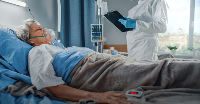 A patient laying in a hospital bed while a doctor stands with a clipboard