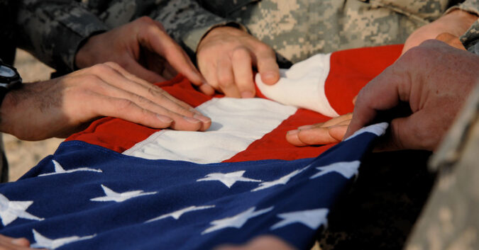 Veterans lay their hands upon a folded American flag