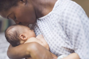 A mother in a hospital gown kissing her newborn's forehead