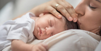 A mother kisses the top of her newborn's head