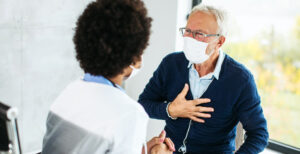 A patient holds his chest while speaking with his doctor