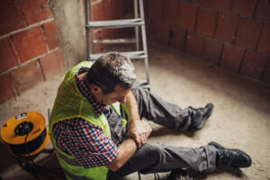 A worker sits on the floor holding his wrist next to a ladder