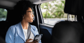 A rideshare passenger holds her phone while looking out the window