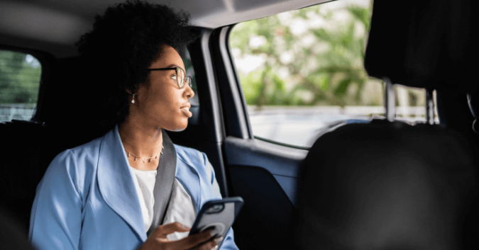 A rideshare passenger holds her phone while looking out the window