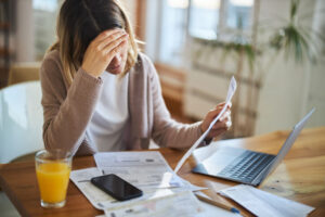 A woman sifts through paper work in front of her computer, visibly frustrated